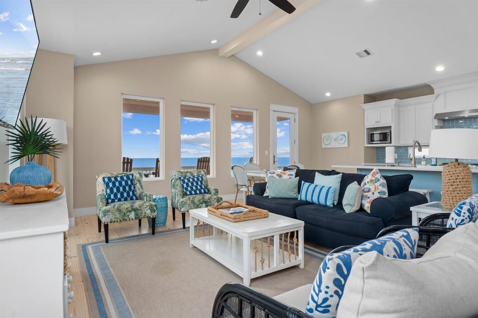 Open-concept living area with modern coastal décor, ample seating, and natural light overlooking the beach.