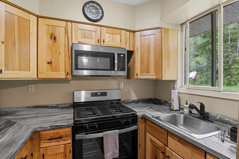 The Main House - Kitchen - Modern kitchen with wooden cabinets, granite countertops, and a window view of lush greenery, perfect for culinary enthusiasts.