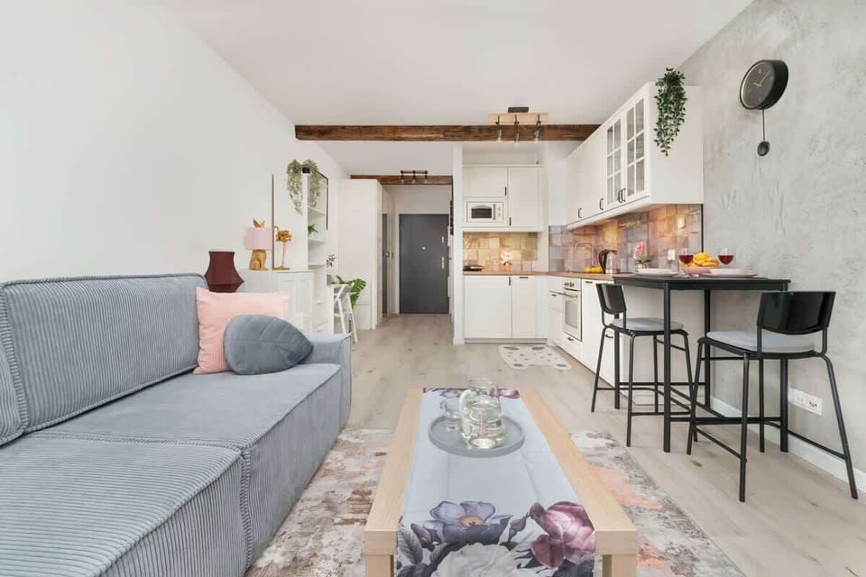 A stylish seating area with a grey sofa, wooden coffee table, and bar stools in the background.

