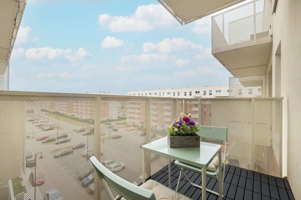 A sunny balcony with a view over residential buildings and parked cars.

