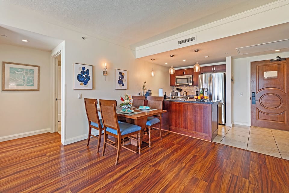 Honua Kai Konea 206’s kitchen and dining area feature rich wood floors and soft lighting.