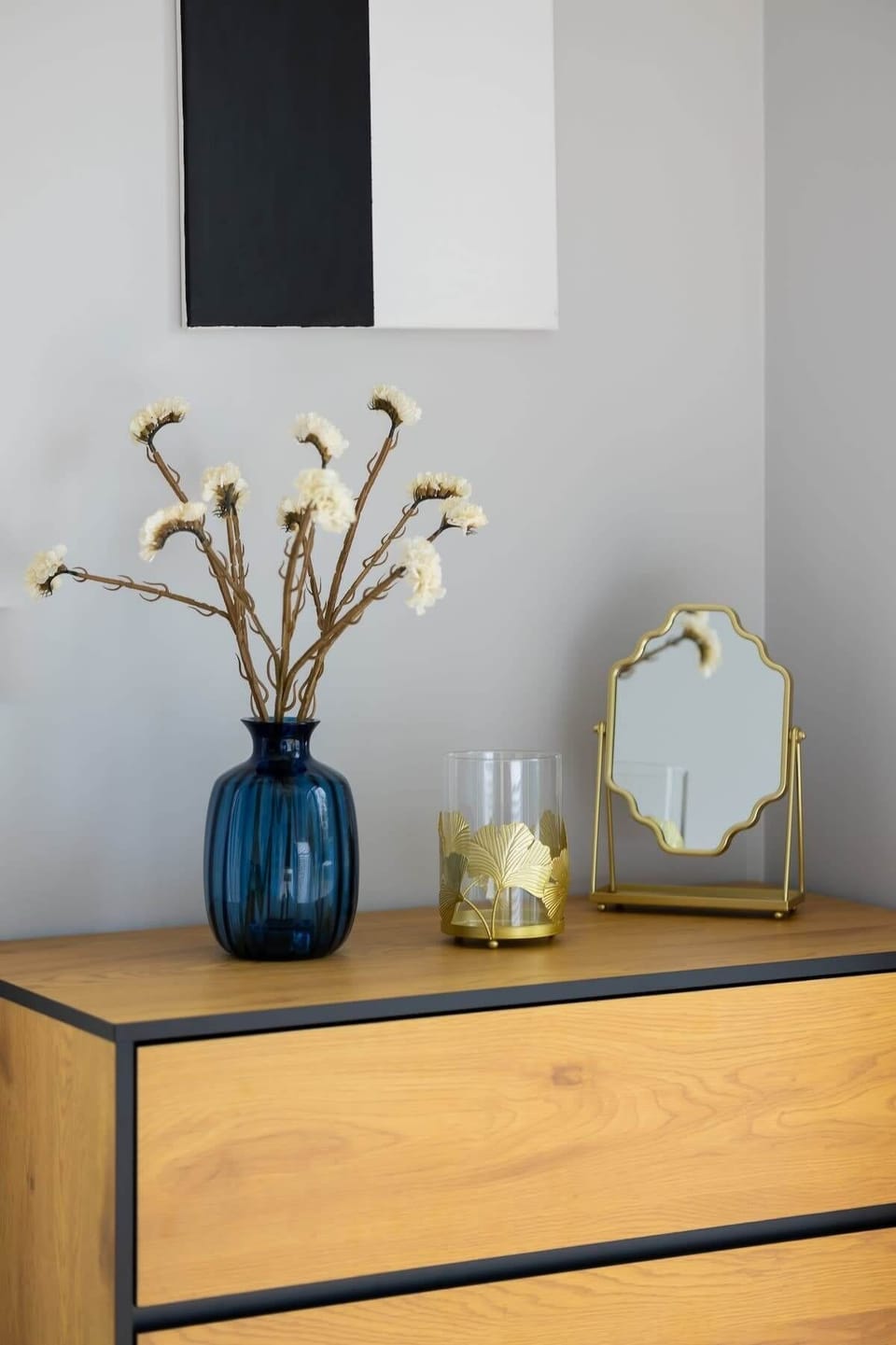 A stylish wooden dresser with elegant decor, including a vase with dried flowers and decorative glass jars, adding a refined touch to the room.