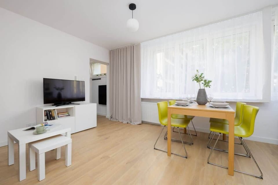 A dining-living area with a TV, white table, and bright natural lighting.

