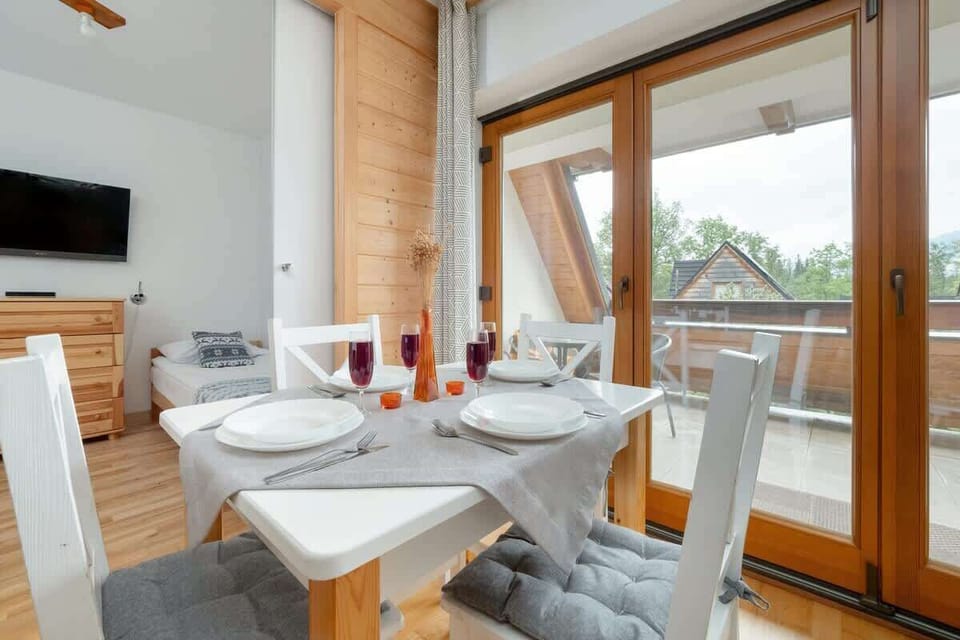 A dining table set for four with a mountain view through large windows and wooden beams.

