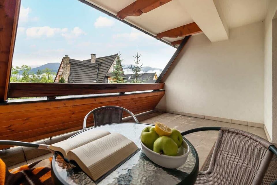 A balcony with a view of rooftops and mountains, featuring cozy rattan seating.


