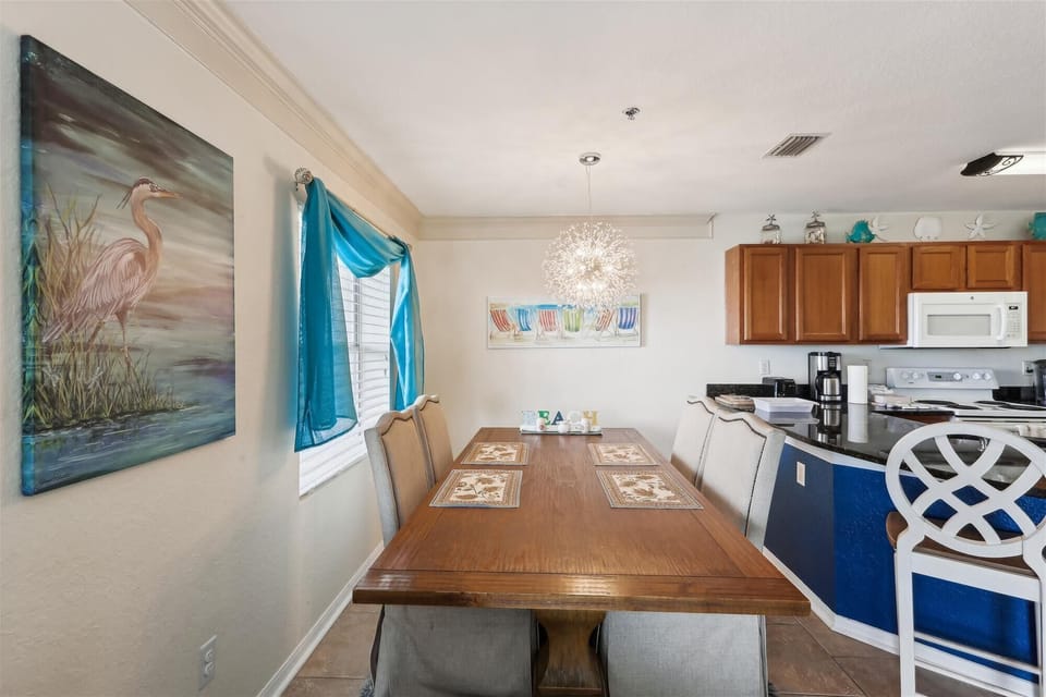 - Elegant dining room with large wooden table and modern chandelier  
- Vibrant coastal artwork and bright drapes enhance cheerful ambiance  
- Ideal for shared meals and special gatherings with family or friends 