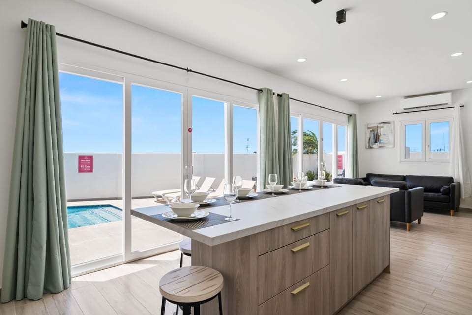 - Open kitchen with island seating overlooking a private pool through floor-to-ceiling glass doors - Natural light floods the space, creating a bright and airy atmosphere - Seamless indoor-outdoor living, perfect for relaxation and entertaining