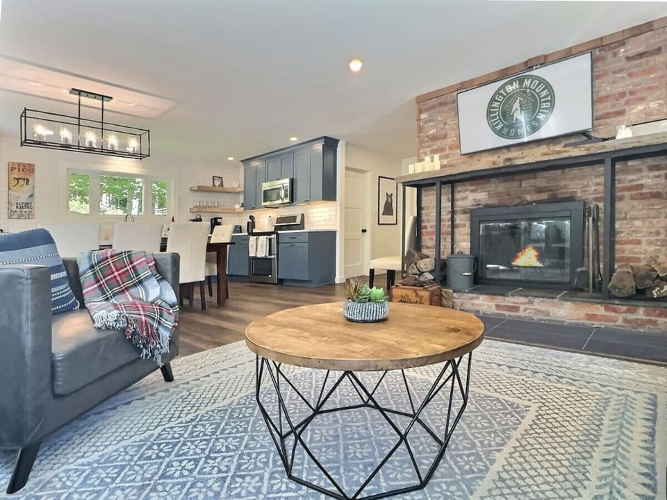Spacious living room with large TV, cozy fireplace, and open flow to the dining area and kitchen.