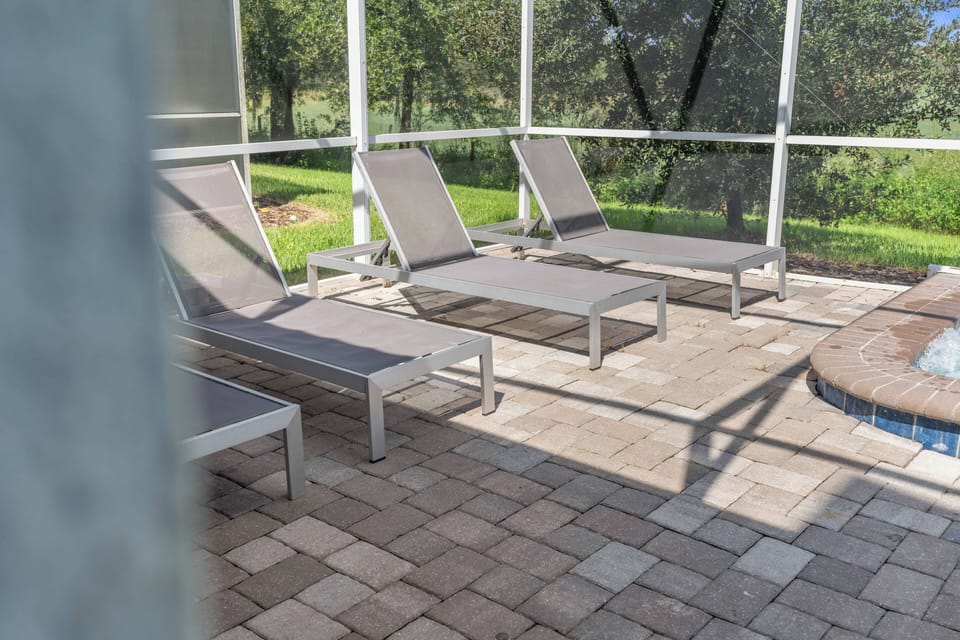 Step outside to a charming patio with sleek lounge chairs ideal for sunbathing. The warm stone pavers create a cozy vibe, while lush greenery adds to your delightful outdoor experience. Enjoy your time in this serene space!