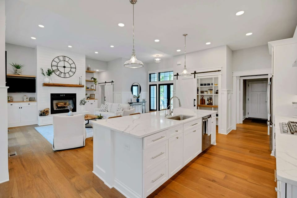 Open-concept kitchen and living area featuring a spacious marble island, modern fixtures, and seamless flow into a cozy, well-lit living room.