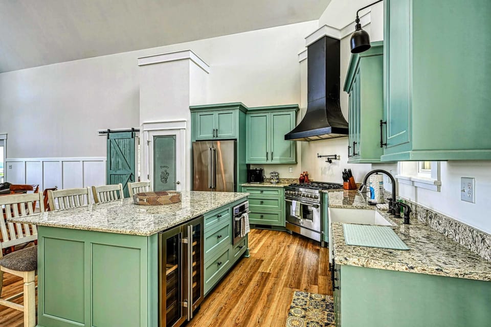 Modern kitchen with a large granite island, wine cooler, and sleek green cabinetry, perfect for preparing and enjoying meals