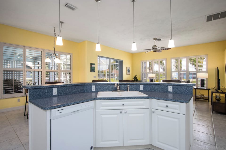Cook, chat, and dine comfortably with an island that features a sink and barstools, overlooking the spacious den and dining area