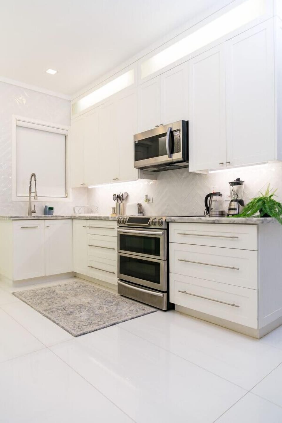 Sleek kitchen w/ white cabinets, stainless appliances & marble-style counters for easy meal prep