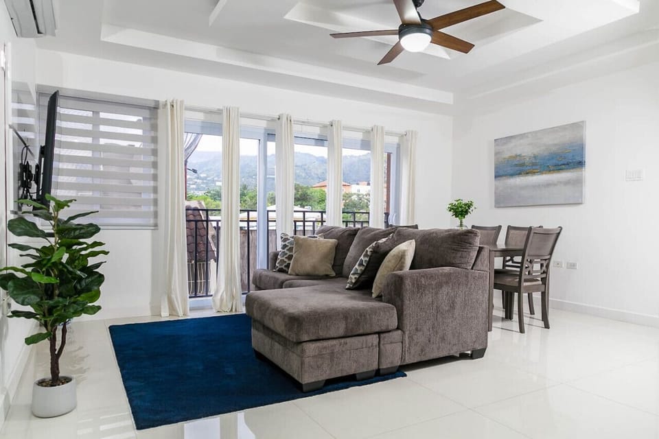 Bright living room w/ plush sofa, dining table & wall of windows letting in natural light