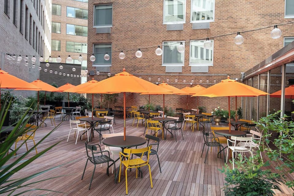 Sip coffee outdoors under umbrellas in a sunny courtyard.