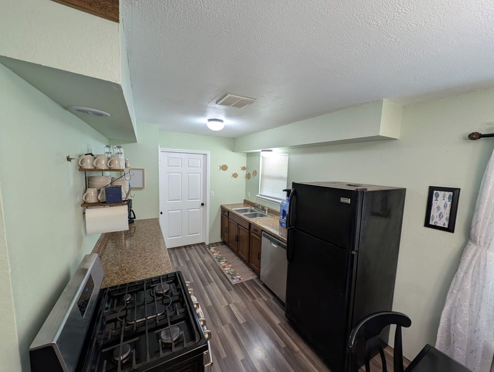 Full kitchen with dishes, cookware, gas stove, oven, refrigerator, & dishwasher.