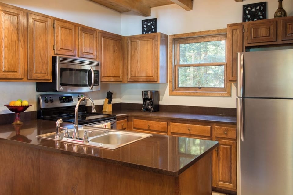 Your fully equipped kitchen offers gleaming appliances, warm wood cabinetry, and ample counter space for preparing meals. Sunlight streams through the window, illuminating your home-away-from-home.