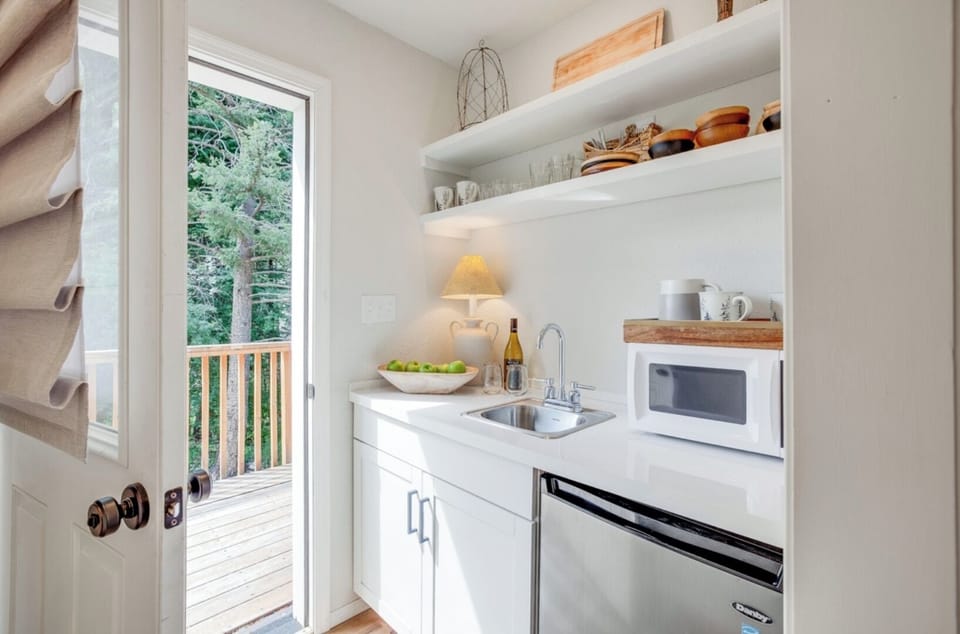 Your own compact kitchenette has everything you need—microwave, mini fridge, and open shelving stocked with dishes for easy meal prep with a view of the trees.