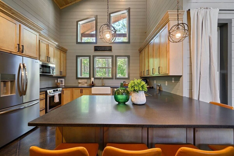 Modern rustic kitchen with stainless steel appliances, large island, and forest view windows – perfect for cozy cabin cooking and entertaining.