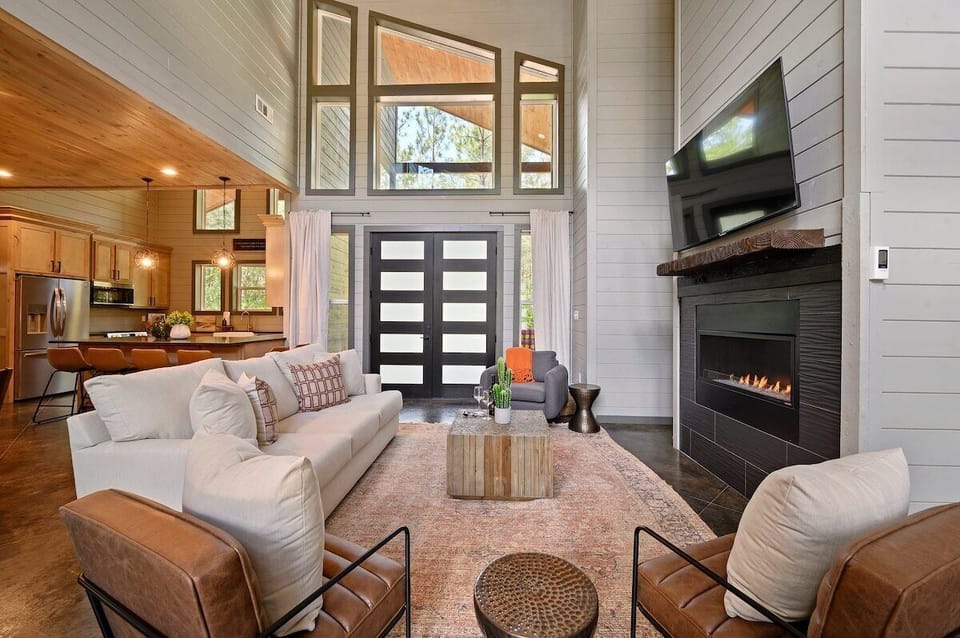 Spacious luxury cabin living room with floor-to-ceiling windows, fireplace, and open concept layout – perfect forest retreat setting.