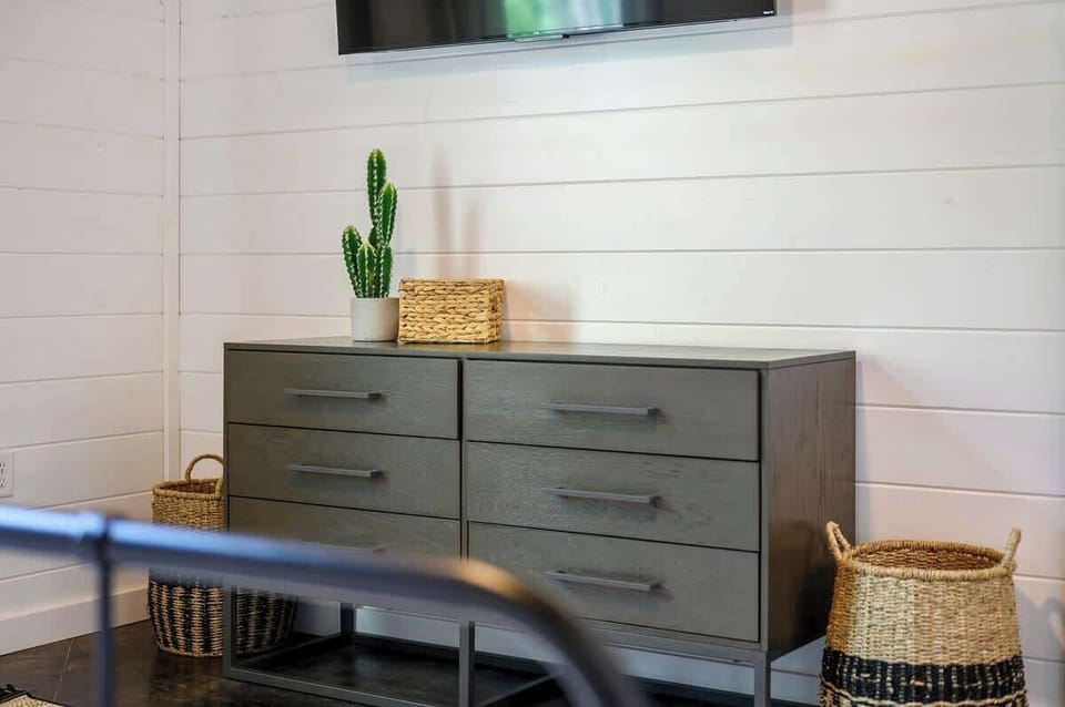 Modern dresser with woven baskets and cactus decor in cozy white-paneled cabin bedroom.