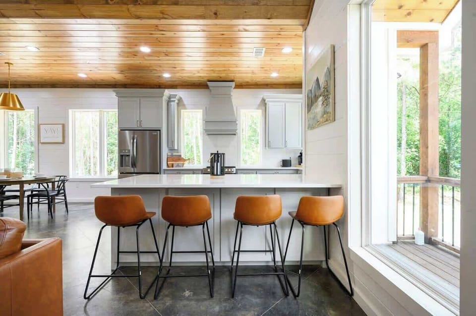 Modern kitchen with island seating, leather barstools, wood ceiling, and stainless steel appliances in luxury cabin rental.