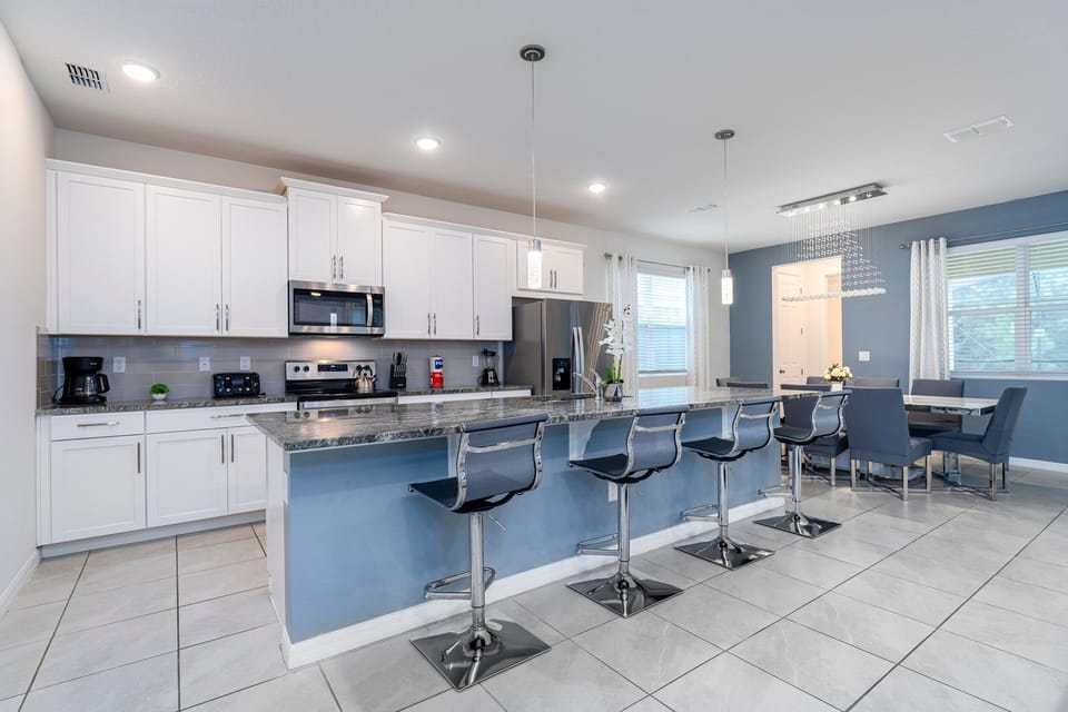 Modern kitchen featuring sleek white cabinets, granite countertops, and stylish bar stools. Bright and inviting with ample natural light.