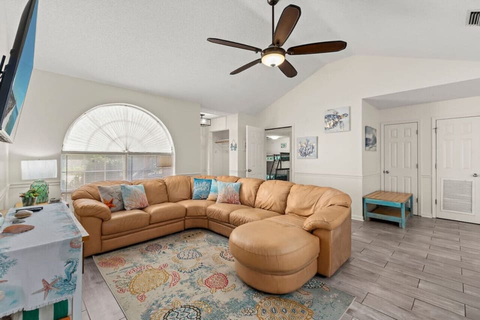 A spacious living room with tall ceilings, a comfortable leather sectional, and a beach theme, filled with natural light and an open, airy feel.