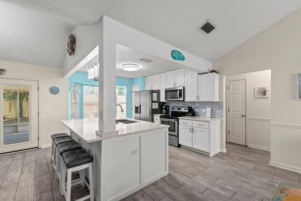 A bright central kitchen with a sleek breakfast bar, outdoor access, and a vibrant turquoise accent wall adding a pop of color.