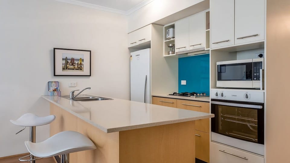 Sleek and functional—enjoy an expansive white stone island bench, ample cabinetry, and a full-sized refrigerator, all set within a clean, contemporary layout.