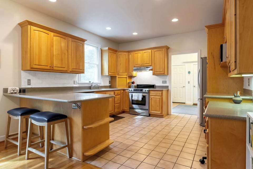 Kitchen with two bar stools, large refrigerator, oven,  microwave and dishwasher