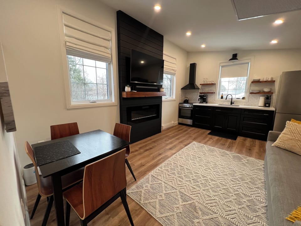 Living area with electric fireplace, entertainment unit and kitchen.
