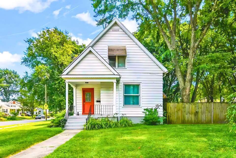 A white home with red accents, nestled in greenery, offers a suburban retreat
