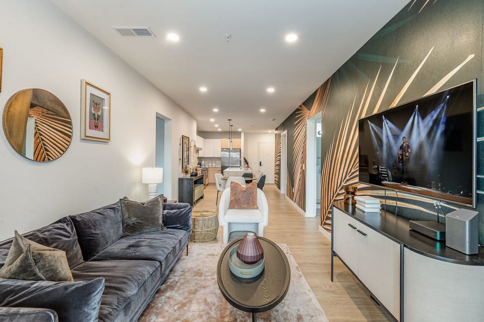 Unit 1: Warm and inviting living space featuring a large flat-screen Smart TV and designer furnishings with a spacious balcony.