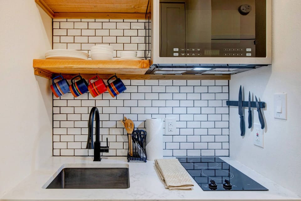Your compact kitchen features subway tile backsplash, stainless appliances, and thoughtful touches like magnetic knife storage and colorful mugs ready for your morning coffee.