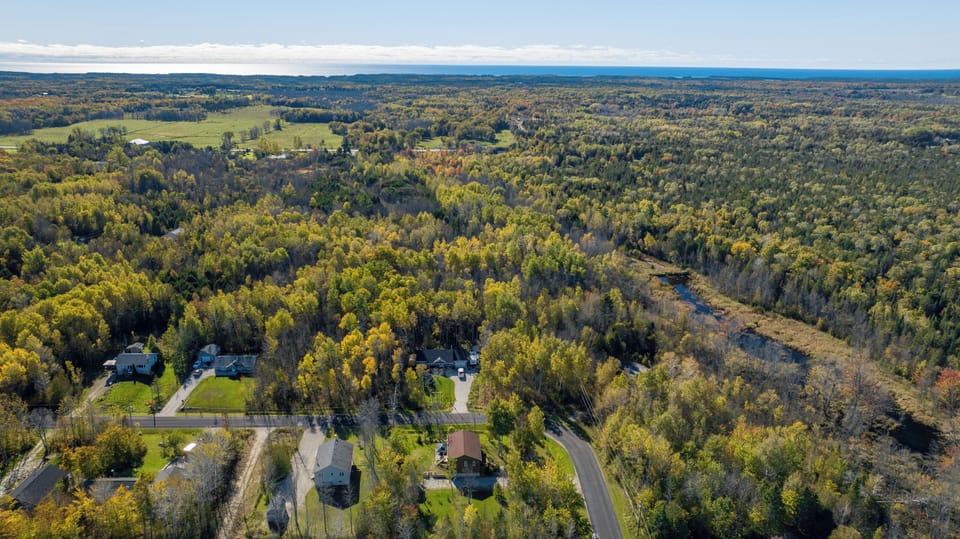 A broader aerial view of the surrounding landscape, showing the mix of open fields, forests, and distant lake views. Black Bear Cottage is perfectly situated for guests looking to immerse themselves in nature while still being close to local amenities and attractions.
