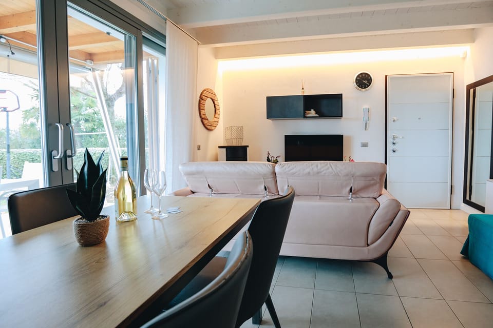 Modern and bright living room with large windows, dining area, and direct access to the outdoor patio, ideal for relaxing moments in Peschiera del Garda.