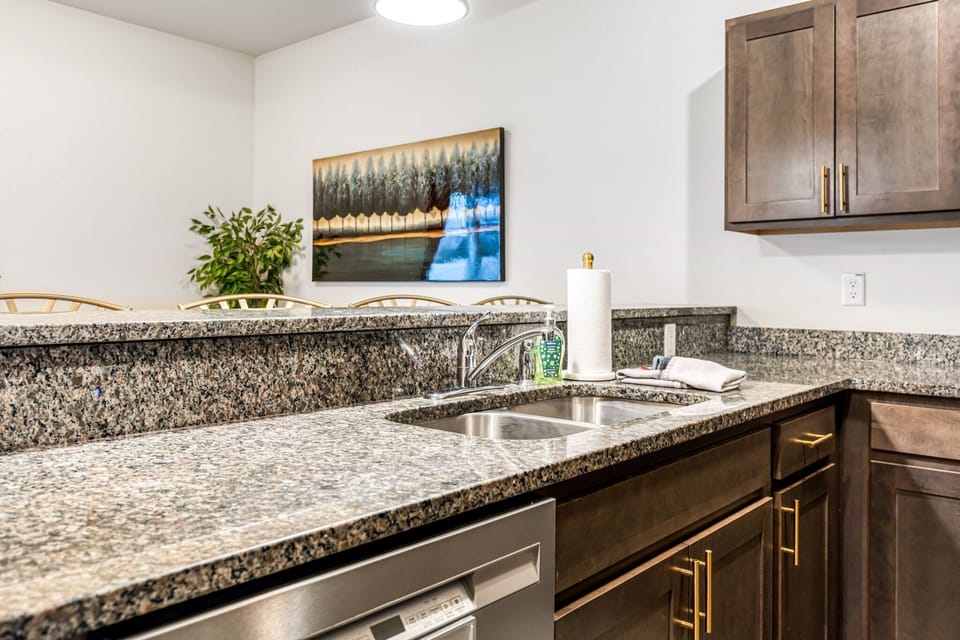 The kitchen sink area pairs stone countertops with an under-mount sink, dishwasher, and ample lower cabinetry.