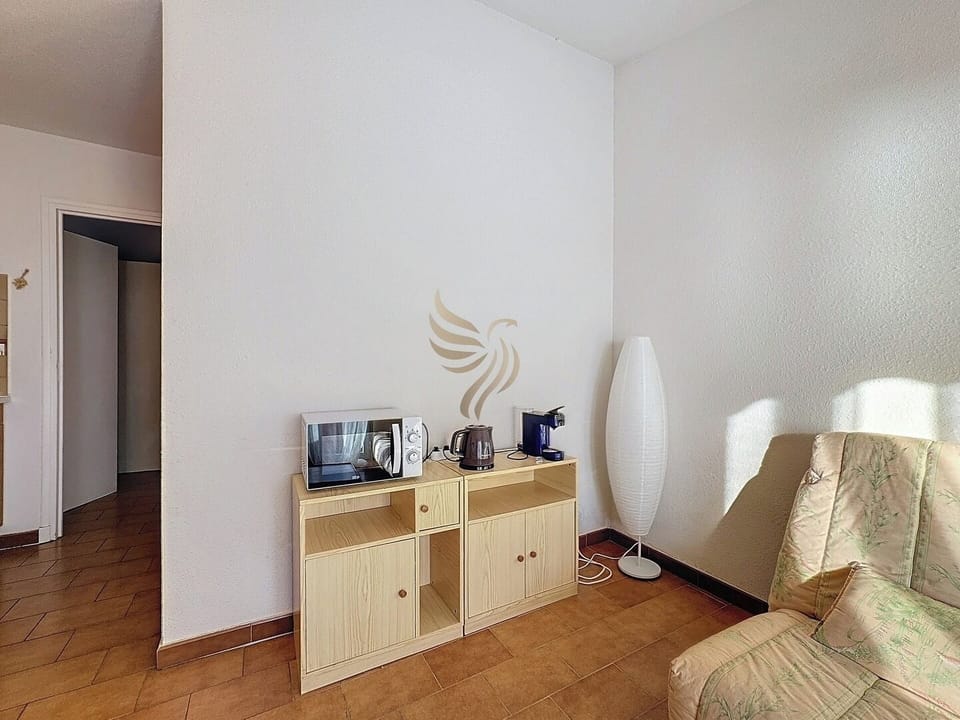 Ce salon offre un espace cosy pour se détendre. Le lampadaire diffuse une lumière douce, idéale pour lire ou se reposer le soir. Un coin pratique pour se préparer un café ou un thé à tout moment de la journée.