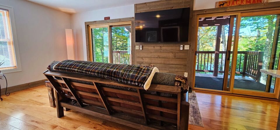 Cozy living area with a futon, large TV, and sliding glass doors leading to a private deck with wooded views.