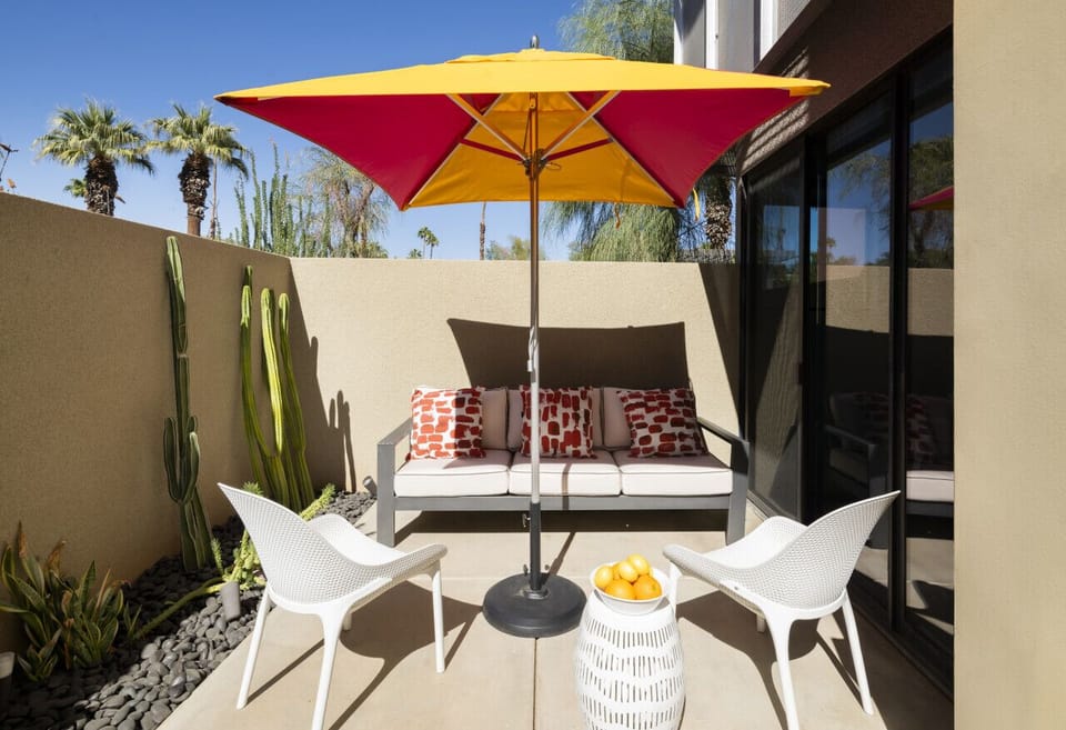 Bask in the Desert Sun! ☀️🌵 This vibrant patio is the perfect spot to sip your morning coffee or unwind in the afternoon glow. Framed by cacti and shaded by a bold umbrella, this private retreat is where comfort meets style in the heart of Palm Springs. #