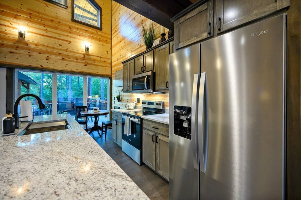 Bright and airy kitchen with granite countertops, stainless steel appliances, and large windows that bring in natural light and views of the surrounding woods. This space perfectly blends functionality with a touch of rustic elegance.