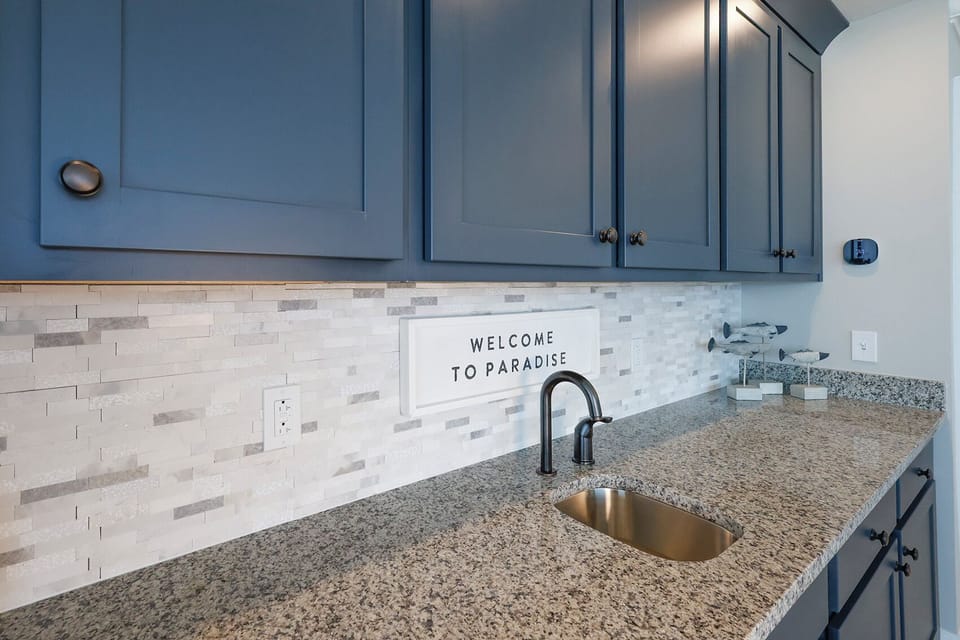 Pour a drink or grab a snack from the wet bar with stylish navy cabinetry and a sleek tile backsplash