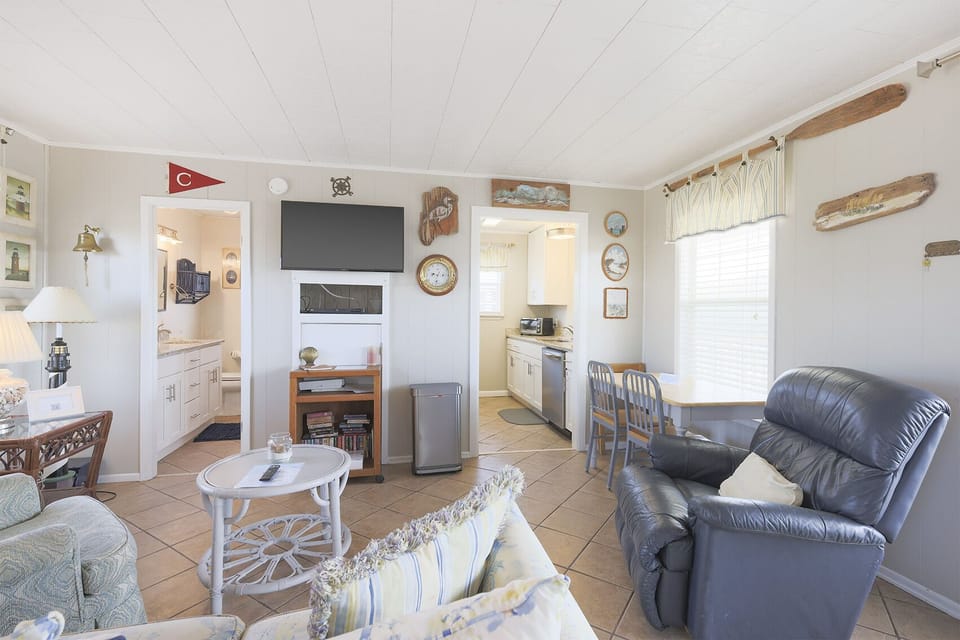 The cozy living area features a TV, charming decor, and a view into the bright kitchen, perfect for relaxation and gatherings