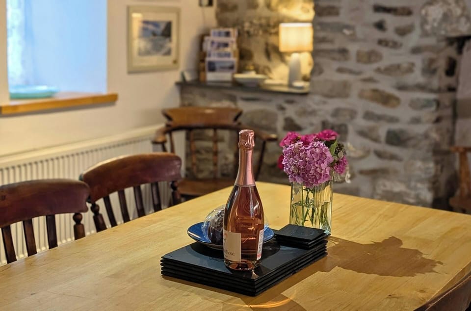 Dining table with bottle, glasses and flower vase, stone wall in background