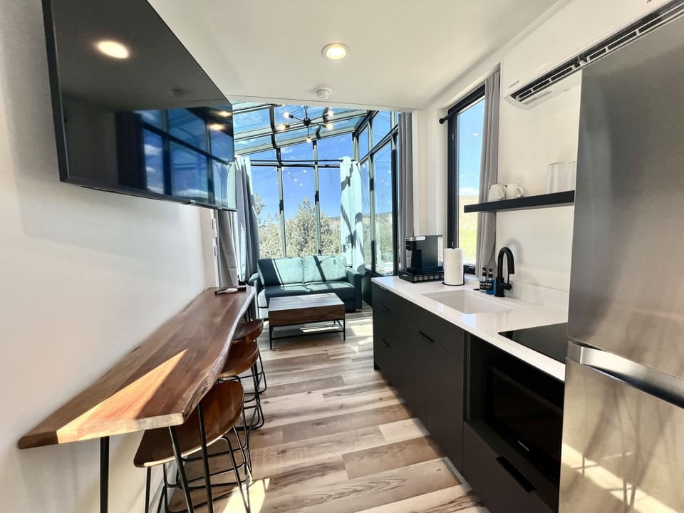 Flat-screen TV, sofa bed, and 360 picture windows inside Stargazer, creating a cozy living space with beautiful Southern Utah views.