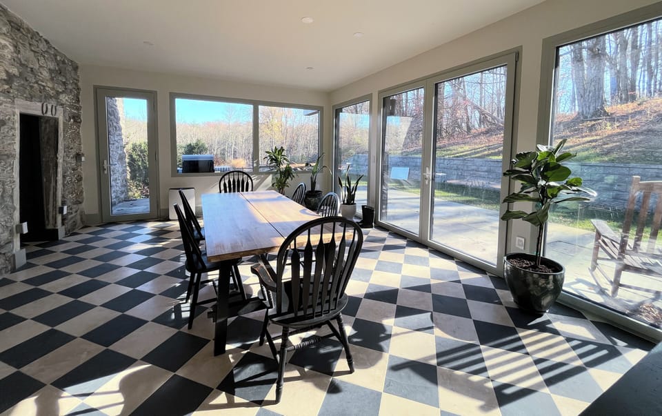 Sun-drenched dining room with stone wall, Italianate floors, and views of forest
