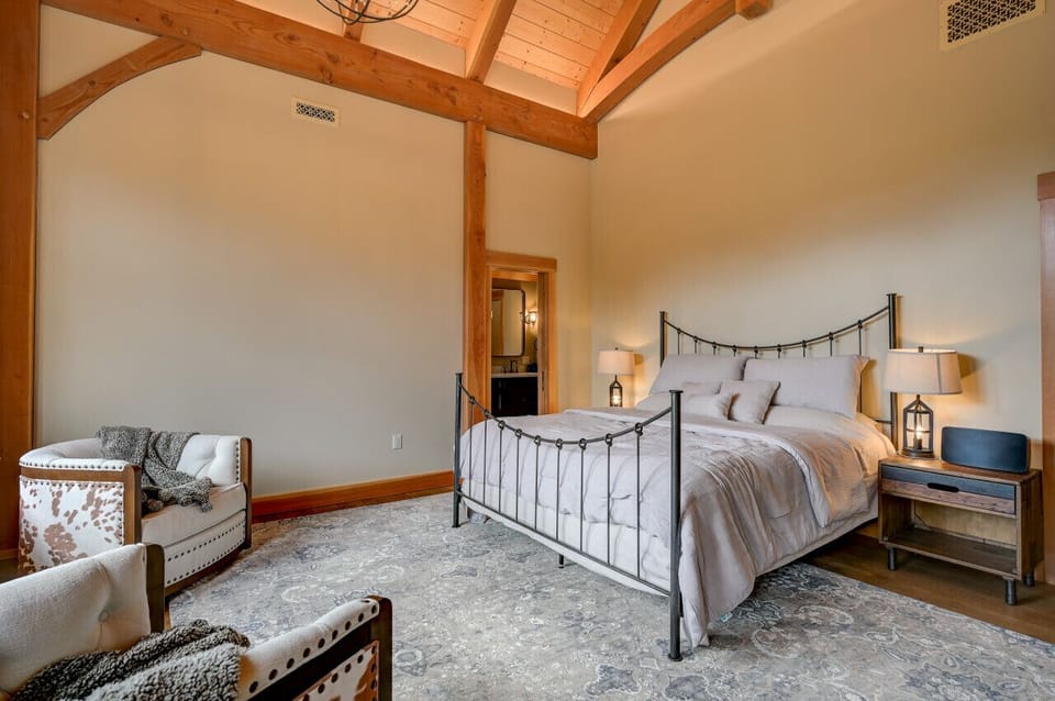Luxurious master suite with a king-sized bed, ensuite bathroom, and breathtaking mountain views. Thoughtfully designed with cozy seating, post-and-beam charm, and charging cables on the nightstands.