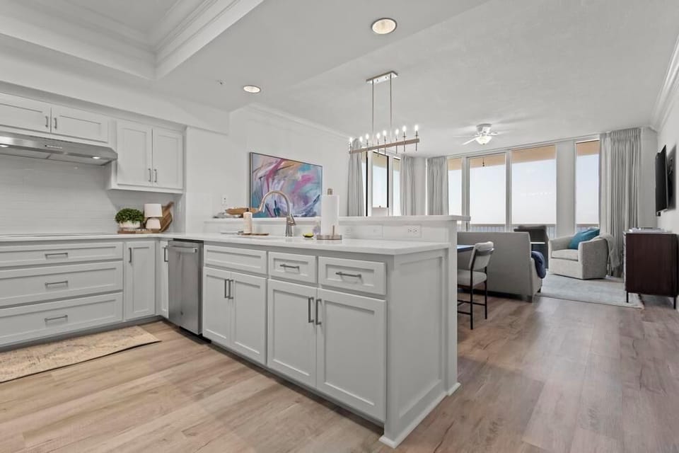 The modern kitchen features stylish white cabinetry, stainless appliances, and a view of the living area with large windows
