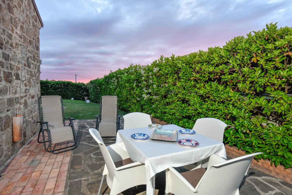 Charming outdoor space: lush hedges, stone table, reclining chairs, soft light.